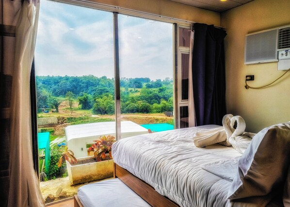 Une chambre d’hôtel avec une grande fenêtre, un lit avec une literie blanche et une vue sur un paysage verdoyant.