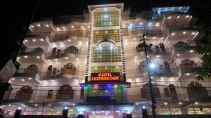 A multi-story hotel with balconies, a prominent sign reading "HOTEL CHITRAKOOT," and a brightly lit entrance.