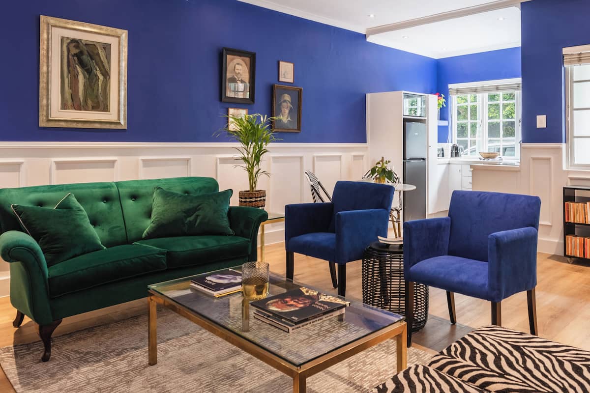 A living room with a green sofa, blue armchairs, a glass coffee table, and a zebra-patterned rug.