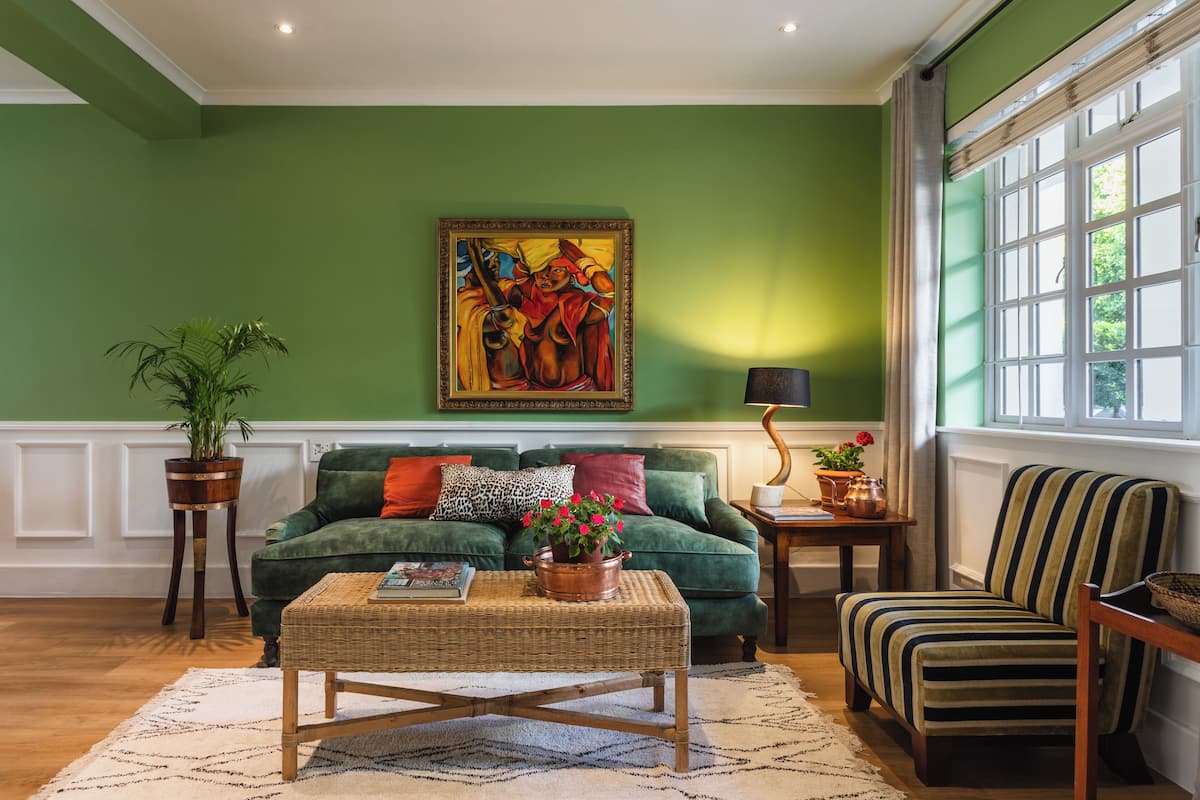A green-walled living room with a green sofa, a striped armchair, a coffee table, and a painting on the wall.