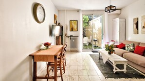 A living room with a dining area, a sofa, a coffee table, a TV, and a large window.
