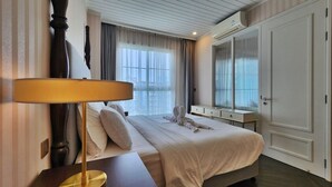 A hotel room with a large bed, a bedside table with a lamp, a dresser, and a large mirror. - Grand Florida 1Bedroom CloseToBeach G601 (Sattahip)