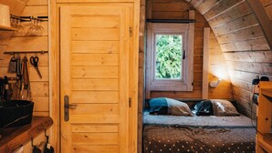 A cozy wooden cabin bedroom with a bed, a window, and a kitchenette. - L'annexe (Sonnay)