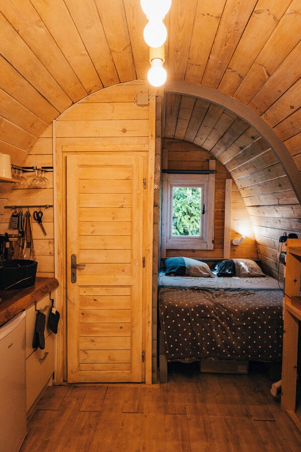 A cozy wooden cabin bedroom with a bed, a window, and a kitchenette.