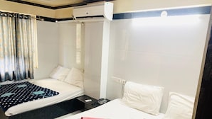 A hotel room with two beds, a bathroom, and a window with curtains. - Hotel Churu Palace (Jaipur)