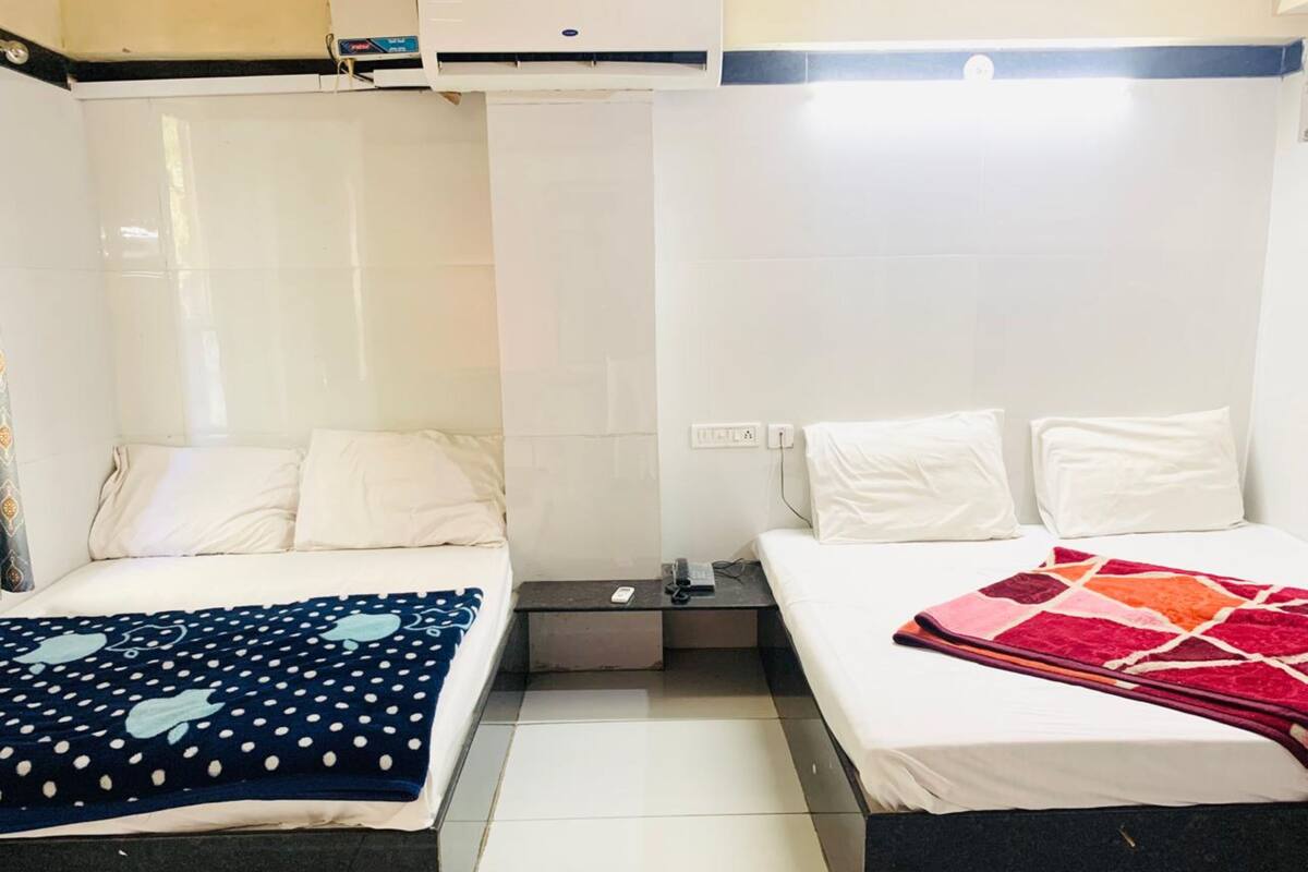 Une chambre d’hôtel avec deux lits, chacun étant équipé de draps blancs et d’une couverture à motifs différents. Une petite table se trouve entre les lits, sur laquelle reposent une télécommande et un téléphone.