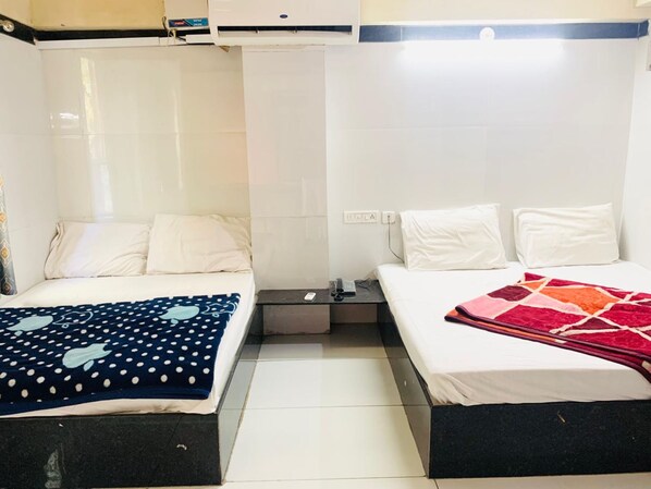 A hotel room with two beds, each with white bedding and a different patterned blanket. There is a small table between the beds with a remote control and a phone. - Hotel Churu Palace (Jaipur)