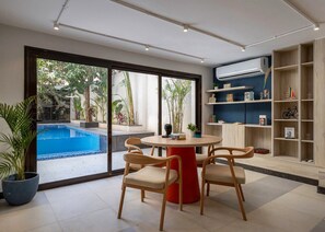 A modern living room with a pool view, a round red table, and wooden chairs.