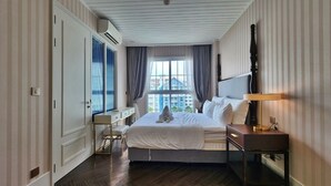A hotel room with a bed, bedside table, lamp, and a view of buildings through the window. - Grand Florida 1Bedroom CloseToBeach G610 (Sattahip)