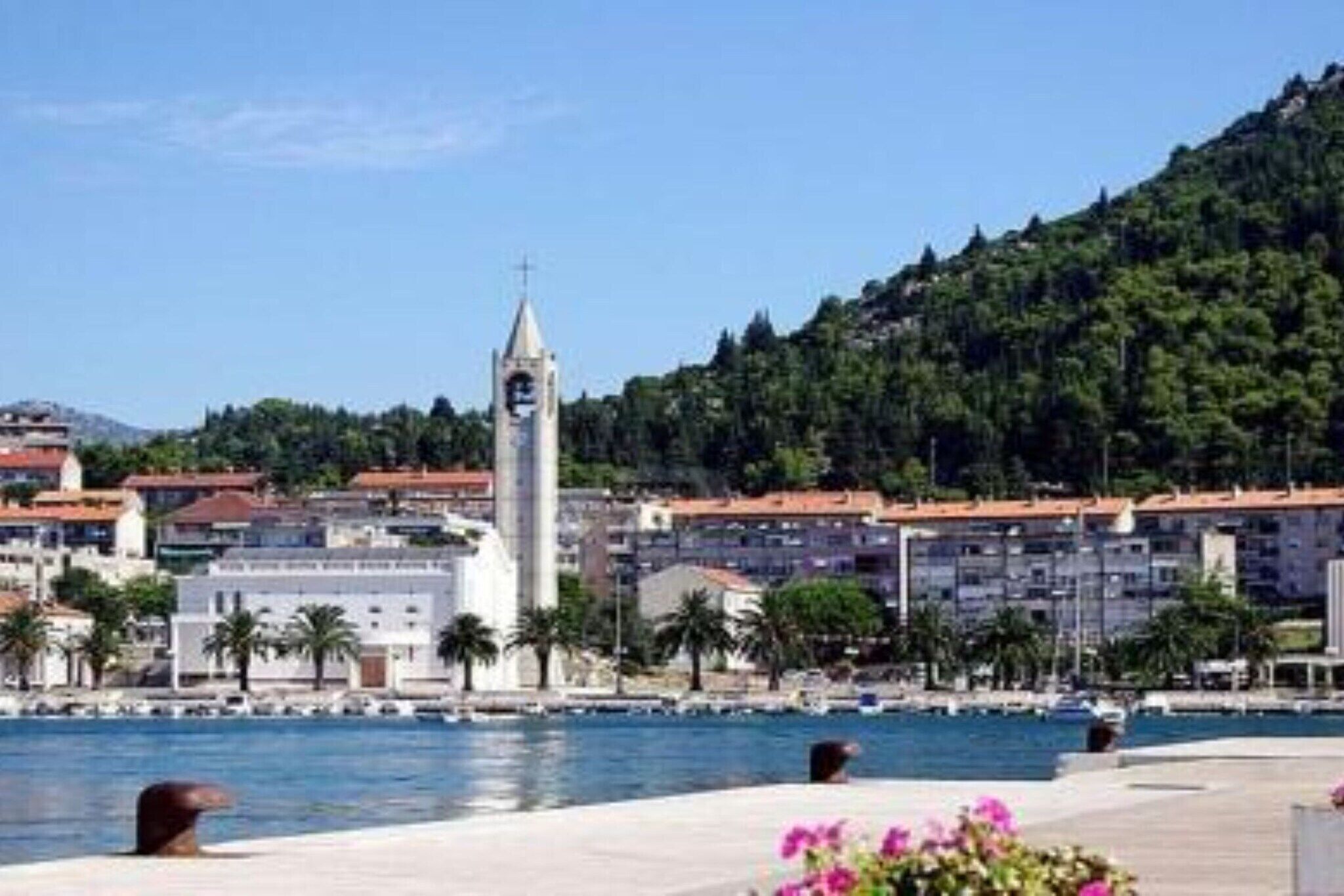 Un pueblo costero con una imponente torre del reloj, un puerto deportivo y edificios con tejados de tejas rojas.