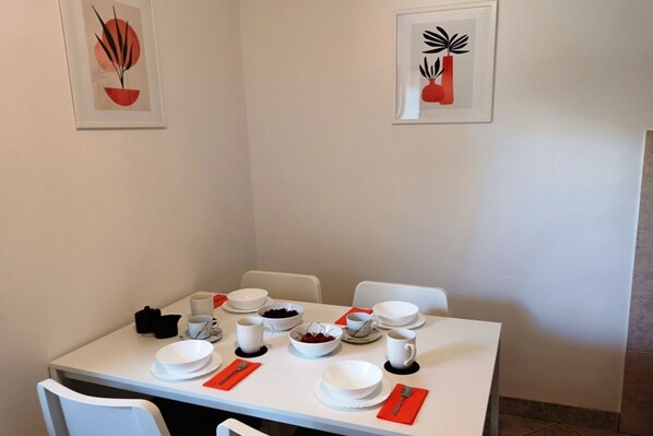 A dining table set with white plates, bowls, and cups, accompanied by red napkins and a black camera. - Two Bedroom Apartment (Povlja)