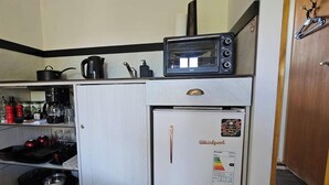 A compact kitchenette with a microwave, kettle, coffee maker, and a refrigerator.