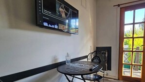 A room with a television mounted on the wall, a table with a bottle, and a door leading to an outdoor area.