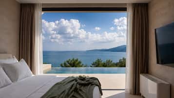 A bedroom with a bed, a TV, and a large window with a view of the sea and mountains.