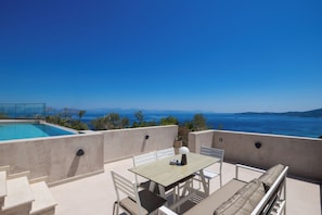 A terrace with a pool, outdoor seating, and a view of the sea.