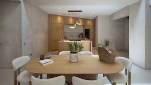 Une cuisine moderne avec des meubles en bois, un îlot central, des luminaires suspendus et un coin repas comprenant une table ronde et des chaises.