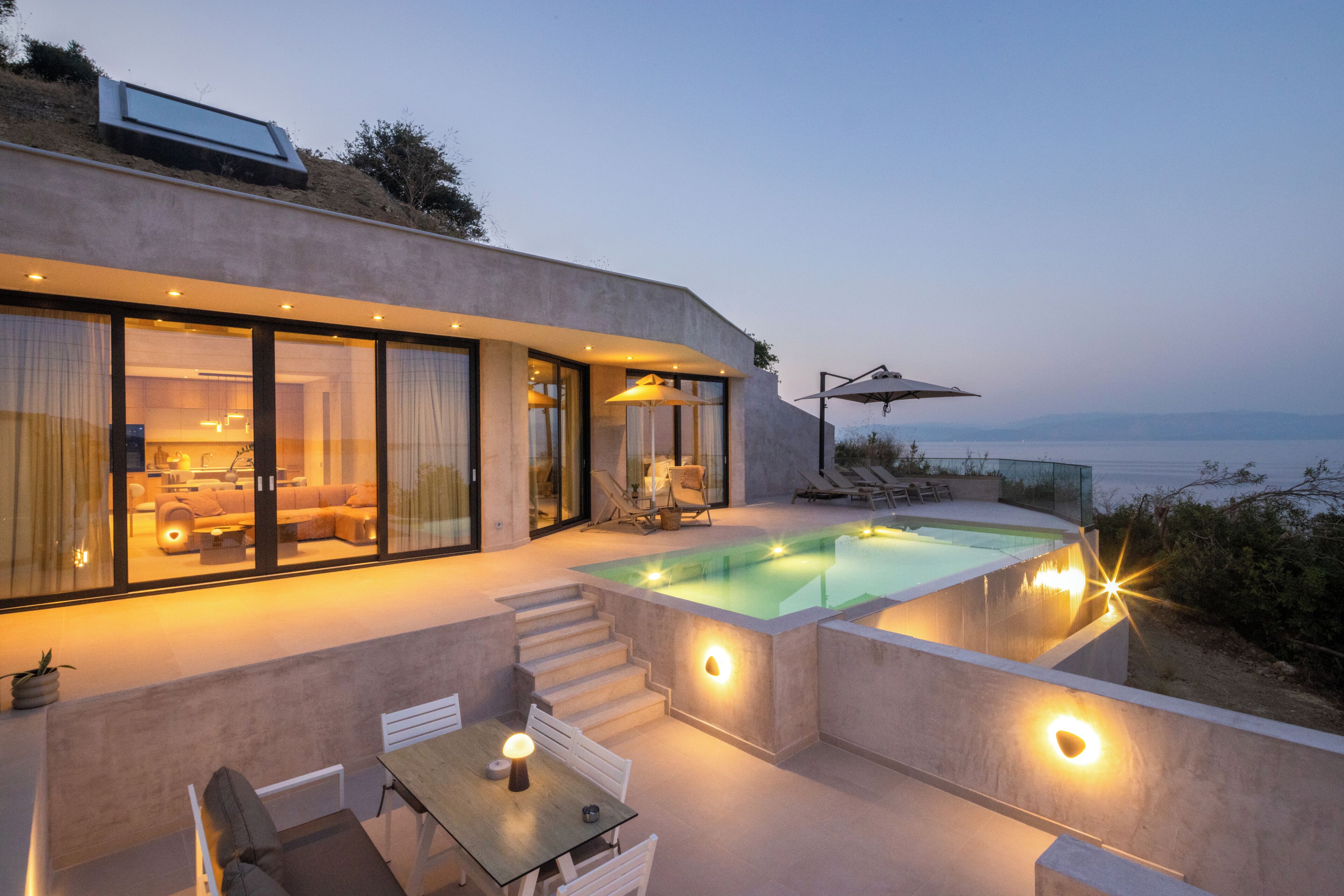 A modern house with a swimming pool, outdoor seating, and a view of the sea.