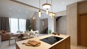 Une cuisine moderne dotée d’un îlot central, de luminaires suspendus et d’un coin repas avec un canapé et des fauteuils.