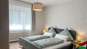 Une chambre à coucher moderne avec un lit, deux tables de chevet, une lampe et une fenêtre avec des rideaux.