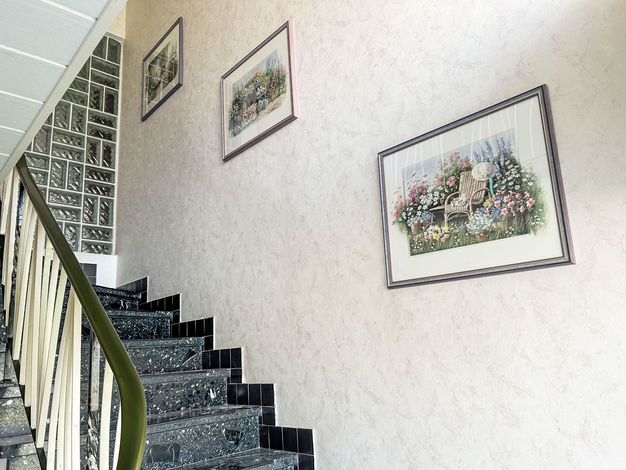 Eine Treppe mit schwarz-weißen Fliesen, einem grünen Geländer und drei gerahmten floralen Gemälden an der Wand.