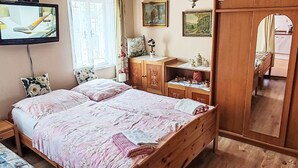 Un dormitorio con cama, armario de madera, televisor y ventana con cortinas.