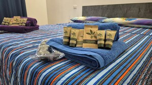 Un letto con una coperta a righe blu e bianche, un asciugamano blu e diversi articoli da bagno, tra cui shampoo, lozione corpo e bagnoschiuma.