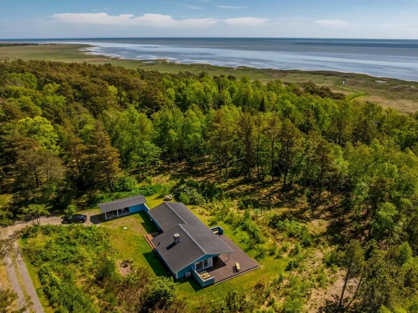 Una casa de dos pisos con un balcón, rodeada de un bosque frondoso y vista al océano.