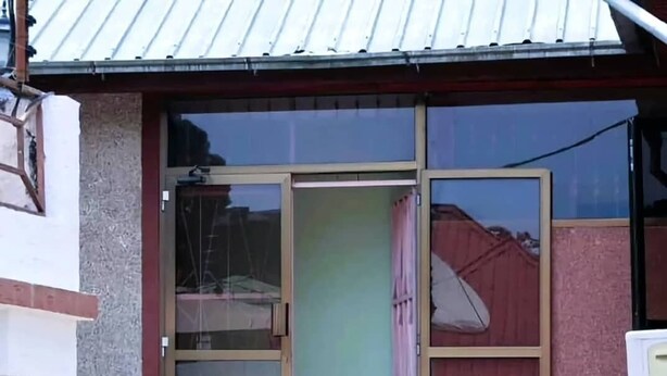 A building with a large glass door, a small set of steps leading to the entrance, and a small garden area with bushes. - Otakef Motel  (Arusha)