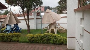 A patio area with outdoor seating and umbrellas, surrounded by greenery and a white building. - Otakef Motel  (Arusha)
