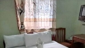 A neatly made bed with white linens, a wooden headboard, and a small bedside table with a lamp. - Otakef Motel  (Arusha)