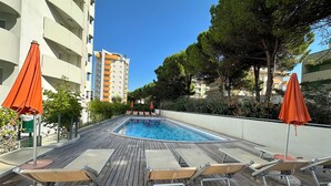 A pool area with wooden decking, lounge chairs, and orange umbrellas. - Apartment With Pool Near the Beach (San Michele al Tagliamento)