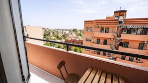 En balkon med et træbord og en stol, der kigger ud over en by med bygninger og palmer.