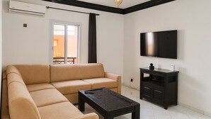 En stue med en beige sofa, et sort sofabord, et fjernsyn på væggen og et lille, sort skab.