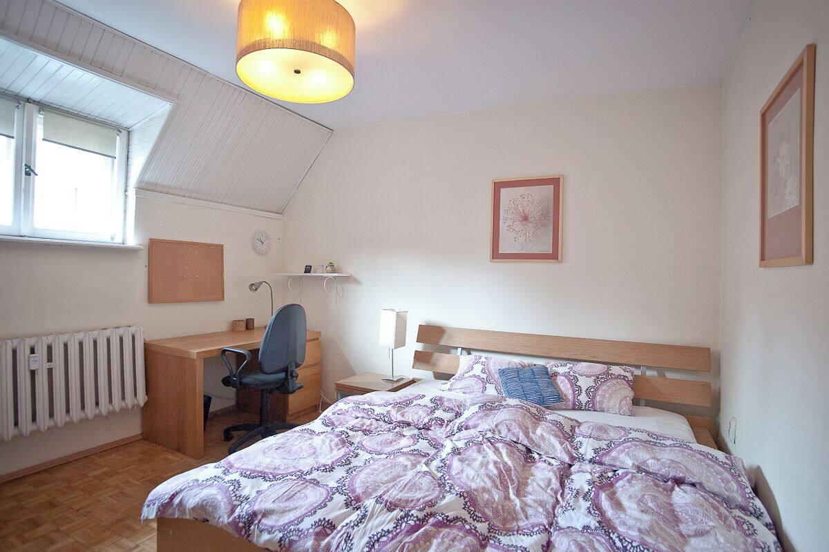 A bedroom with a bed, desk, chair, and a radiator.