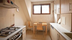 Una cocina con estufa a gas, armarios de madera, una mesa de comedor con sillas y un ventanal con cortinas.