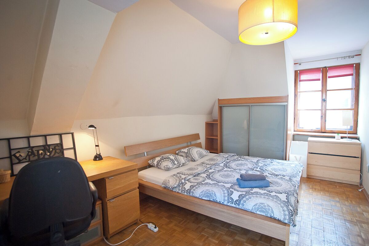 A bedroom with a bed, desk, chair, and a window with curtains.