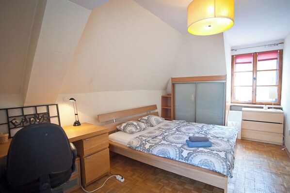 Un dormitorio con cama, escritorio, silla y ventana con cortinas.