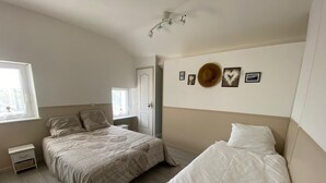 A bedroom with two beds, a window, a bedside table, and wall decorations. - Comfortable apartment 1.5 km from the beach - garden with barbecue (Saint-Vincent-sur-Jard)