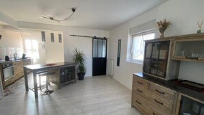 A spacious kitchen with a central island, wooden cabinets, and a large window providing natural light. - Comfortable apartment 1.5 km from the beach - garden with barbecue (Saint-Vincent-sur-Jard)