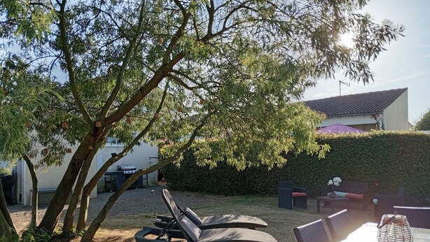 A patio with a table and chairs, surrounded by trees and a hedge. - Comfortable apartment 1.5 km from the beach - garden with barbecue (Saint-Vincent-sur-Jard)