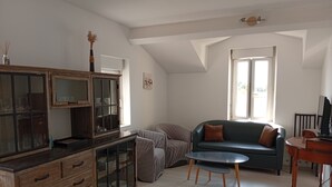 A spacious living room with a high ceiling, a built-in wooden cabinet, a green sofa, and a small round table. - Comfortable apartment 1.5 km from the beach - garden with barbecue (Saint-Vincent-sur-Jard)