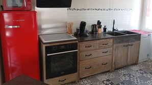 A compact kitchen with a red microwave, a stove, a sink, and wooden cabinets. - Comfortable apartment 1.5 km from the beach - garden with barbecue (Saint-Vincent-sur-Jard)