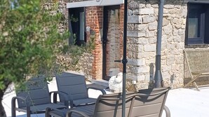 An outdoor patio with a stone building, a table with chairs, and a large umbrella. - Tiny cottage in beautiful Wallonia (Sombreffe)