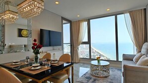A modern hotel room with a dining area, a sofa, and a large window with a view of the sea. - CopacabanaJomtien Condo PrivatePool CBJ1 (Pattaya)