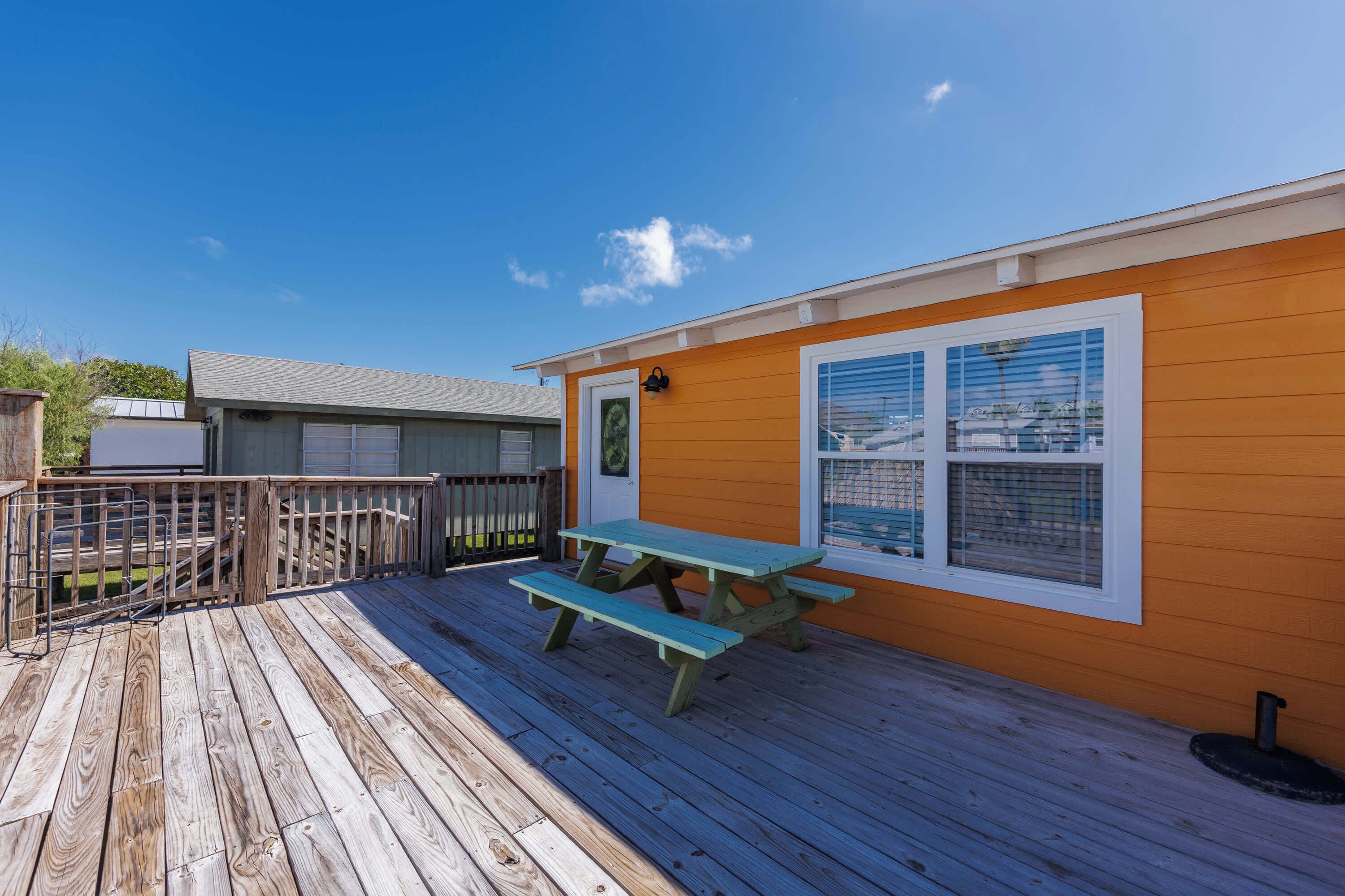 A wooden deck with a picnic table and a small building with orange siding and white trim.