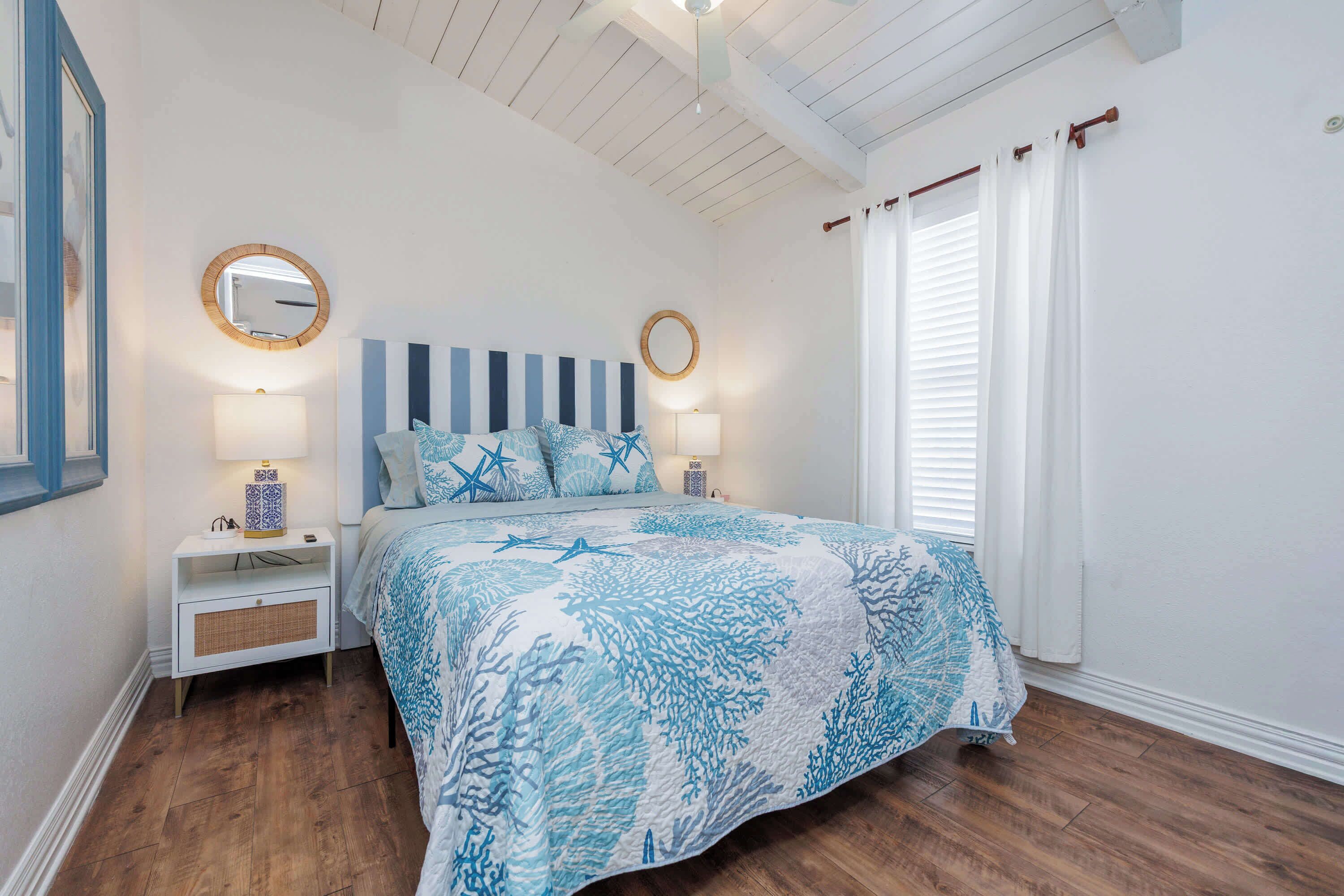 A bedroom with a bed, two bedside tables, a nightstand, a ceiling fan, and a window with curtains.