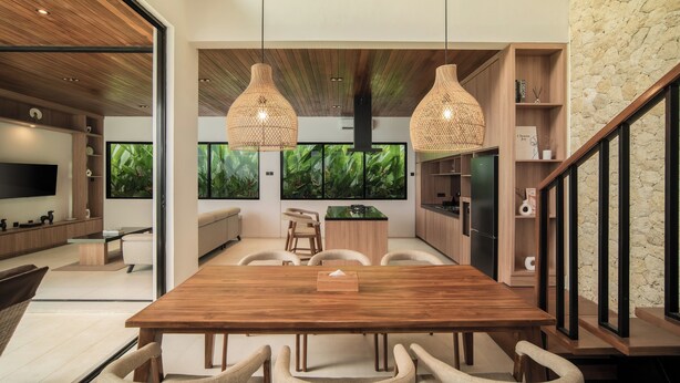 A modern kitchen with a wooden dining table and chairs, a built-in TV, and a large window with a view of greenery. - The Vinava Villa Canggu by Ini Vie Hospitality (Canggu)