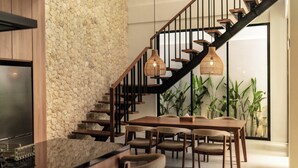 A modern interior with a wooden staircase, a dining area with a table and chairs, and a kitchen with a built-in refrigerator. - The Vinava Villa Canggu by Ini Vie Hospitality (Canggu)