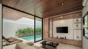 A modern living room with a large TV, comfortable seating, and a view of a swimming pool. - The Vinava Villa Canggu by Ini Vie Hospitality (Canggu)