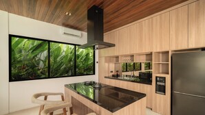 A modern kitchen with a central island, wooden cabinetry, a large window with a plant view, and a stainless steel refrigerator. - The Vinava Villa Canggu by Ini Vie Hospitality (Canggu)